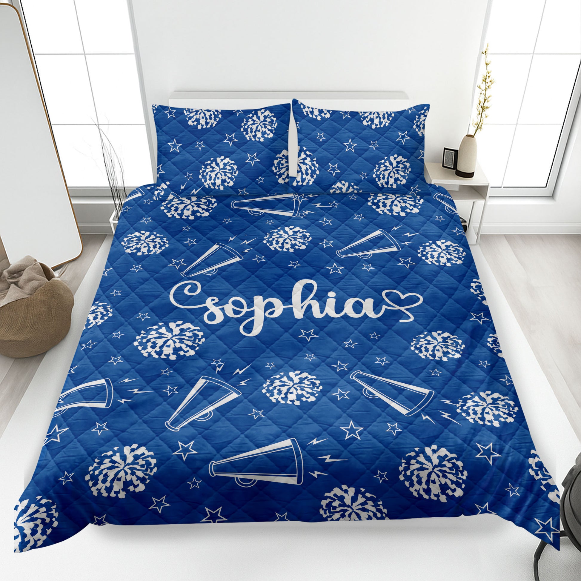 Blue cheerleading quilt blanket displayed on a bed with pom-poms, megaphones, and star accents