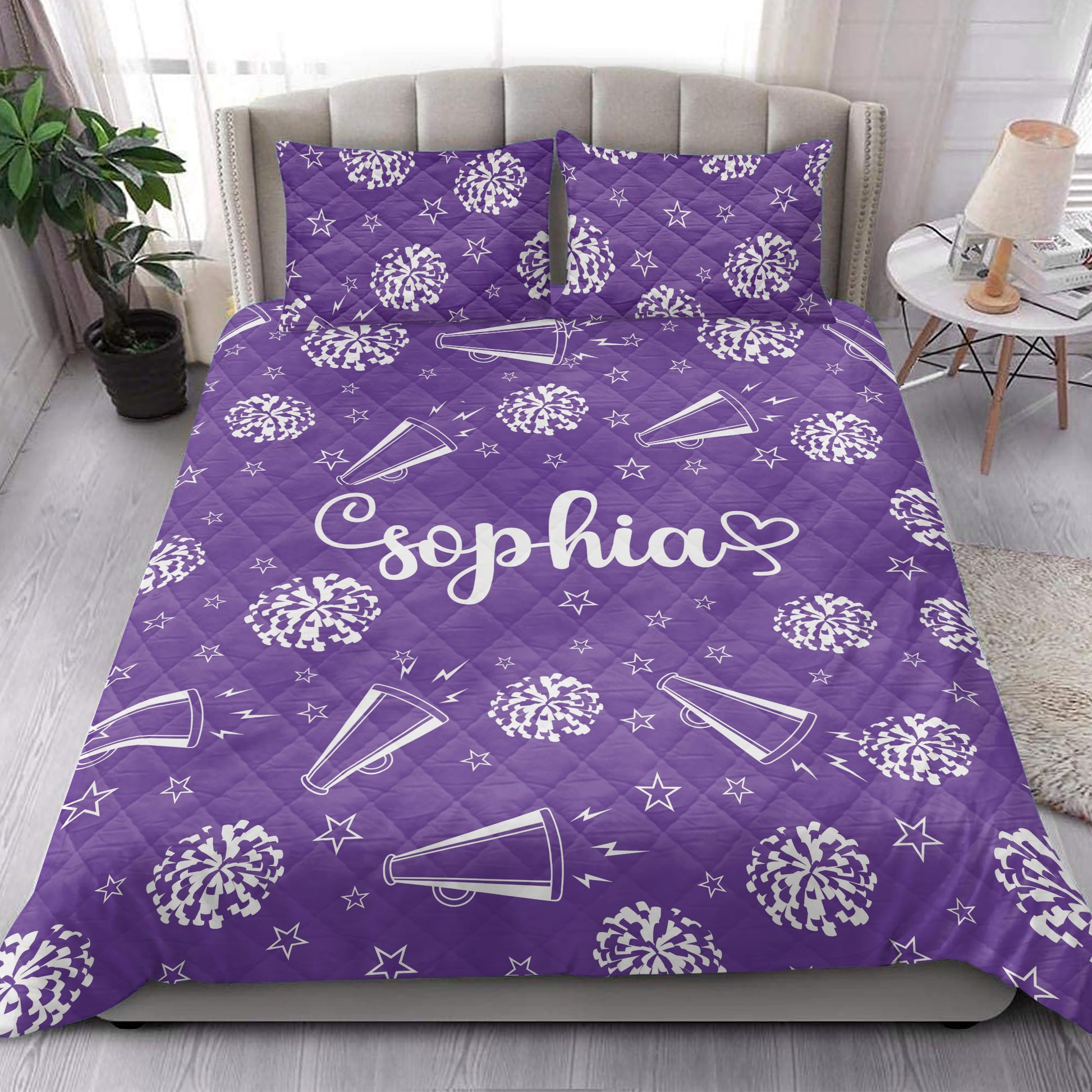 Purple cheerleading quilt blanket shown in a bright bedroom with pom-poms, megaphones, and stars