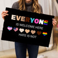 Person holding a black LGBT doormat with colorful hearts and inclusive wording
