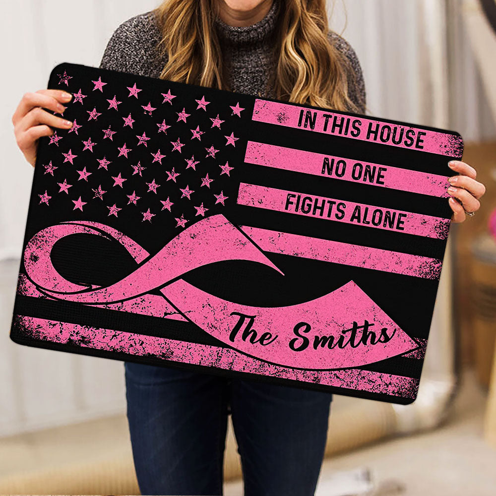 Person holding a black and pink breast cancer ribbon doormat with a solidarity message