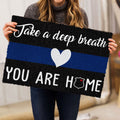 Person holding a police-themed doormat featuring a blue stripe, heart, and badge emblem