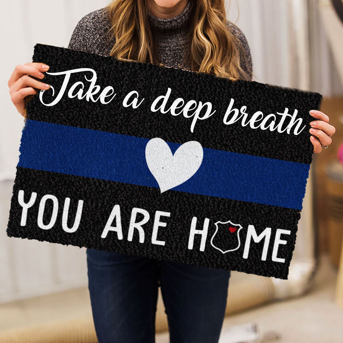 Person holding a police-themed doormat featuring a blue stripe, heart, and badge emblem