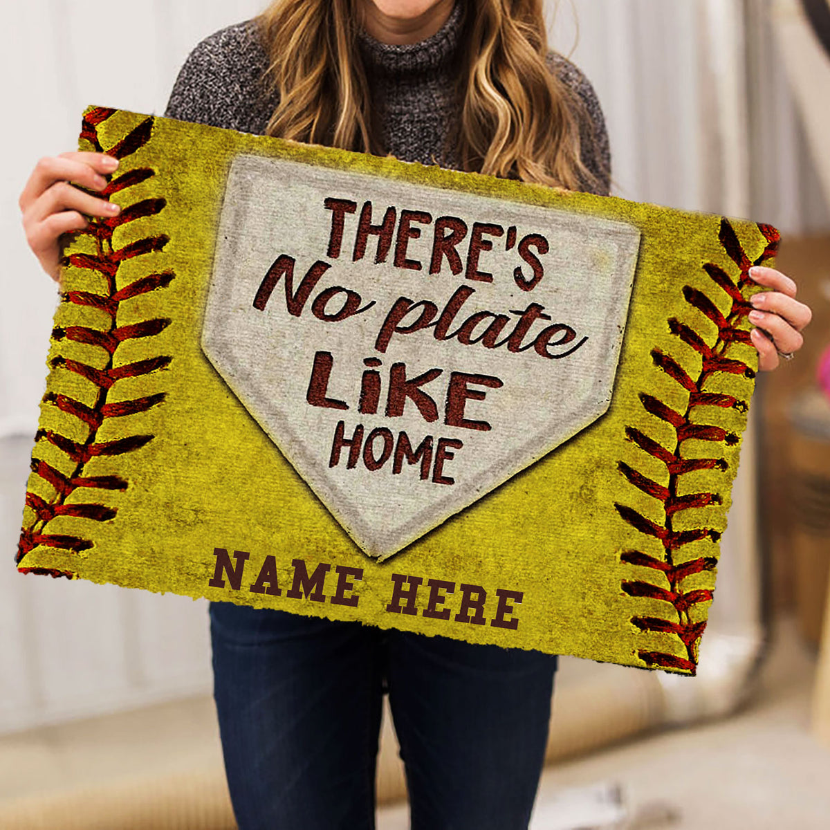 Person holding a yellow softball doormat with home plate artwork and bold entryway lettering