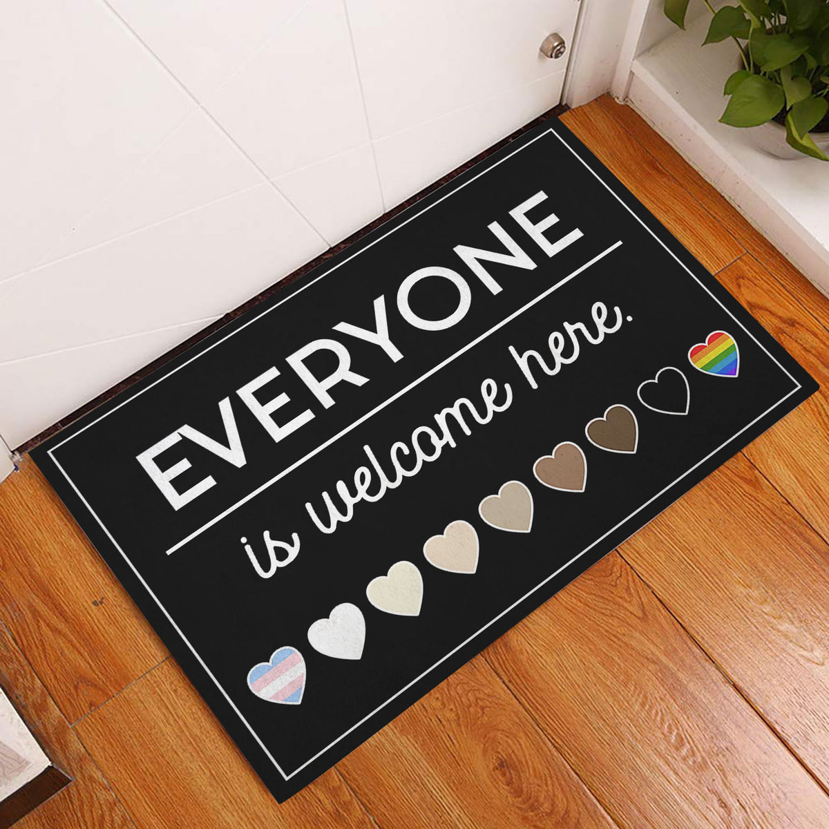 LGBT welcome doormat displayed in an indoor entryway on a warm wood floor