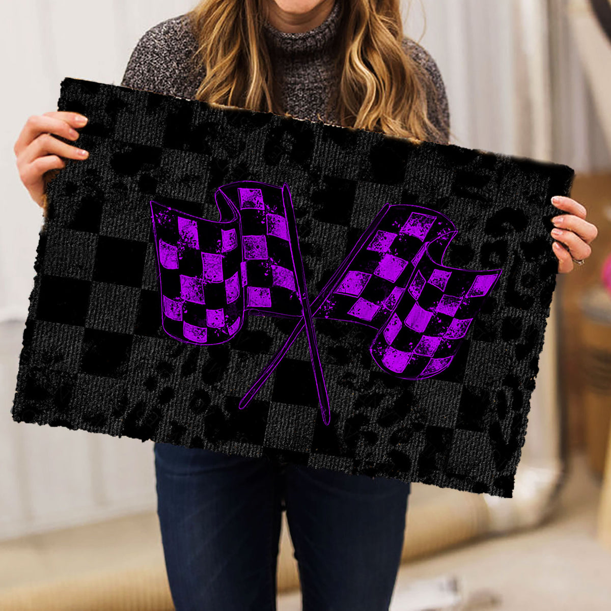 Person holding a racing-themed doormat with crossed purple checkered flags and black checkerboard design