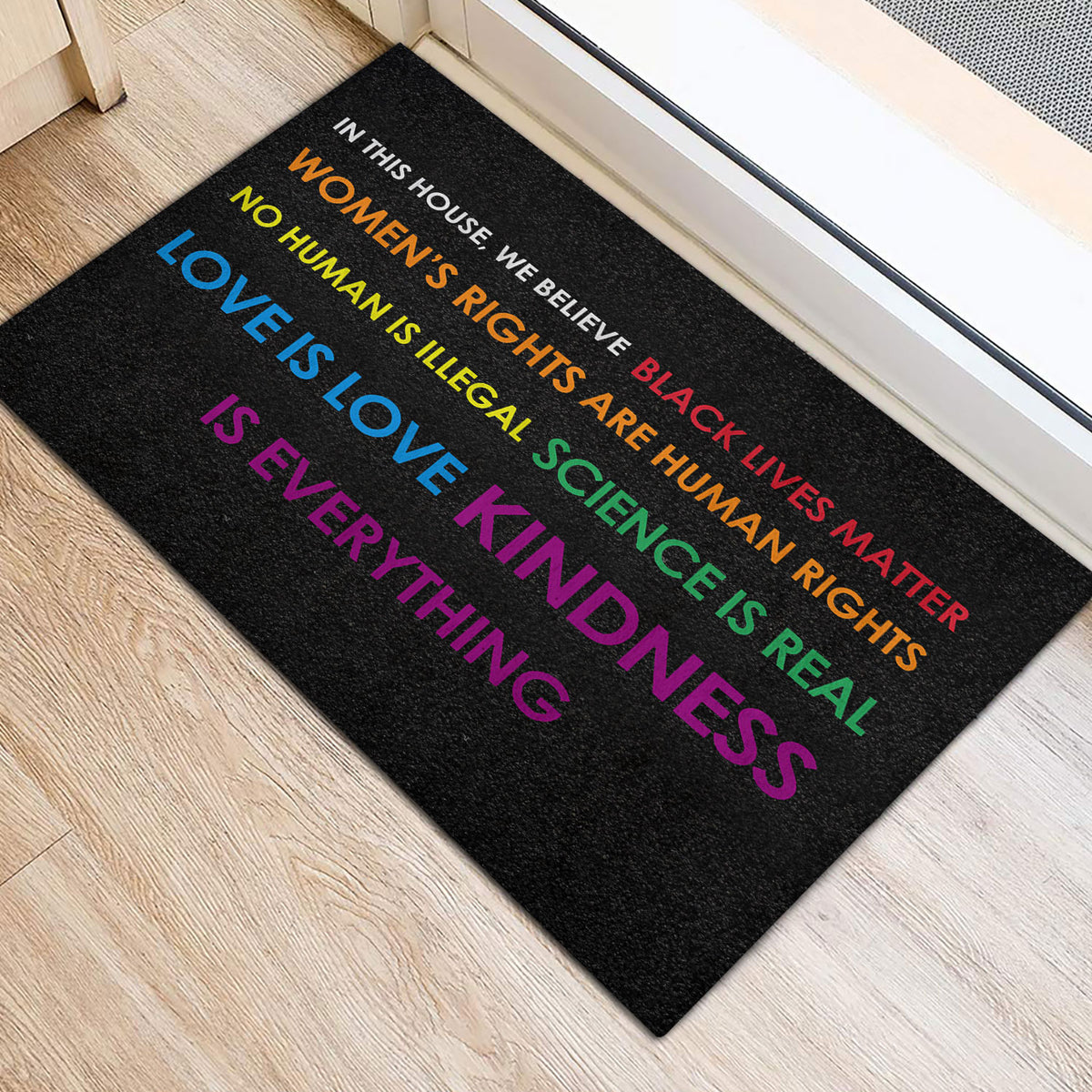 Inclusive LGBT door mat on a light wood floor featuring bold multicolor advocacy text