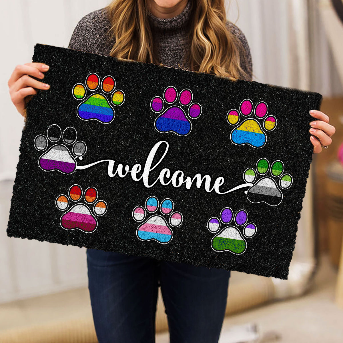 Person holding a black welcome doormat with colorful pride-inspired paw prints