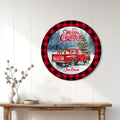 Round Christmas wall sign displayed above a console table with a red vintage truck and decorated tree