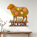 Floral sheep metal wall sign displayed on a white paneled wall above a rustic console table