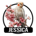 Cockatiel metal sign featuring a detailed bird perched among pink blossom branches in a round black frame