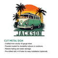 Cut metal sign artwork showing a colorful retro camper van beneath palm trees and a glowing sunset