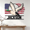 Flying mallard duck hunting wall sign displayed as patriotic decor on a light wood-paneled wall