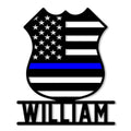 Black police badge metal sign featuring an American flag design with a blue line and bold lower nameplate