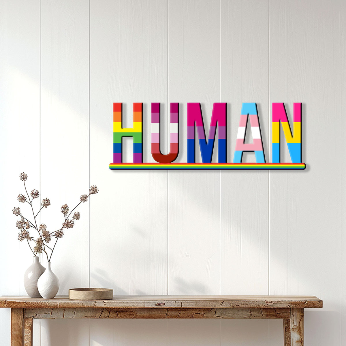 LGBTQ pride HUMAN metal sign displayed on a light paneled wall above a console table