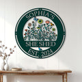 Floral She Shed metal sign displayed on a white paneled wall above a rustic wooden console