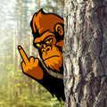 Orange and black gorilla metal sign peeking from behind a tree with a raised middle finger