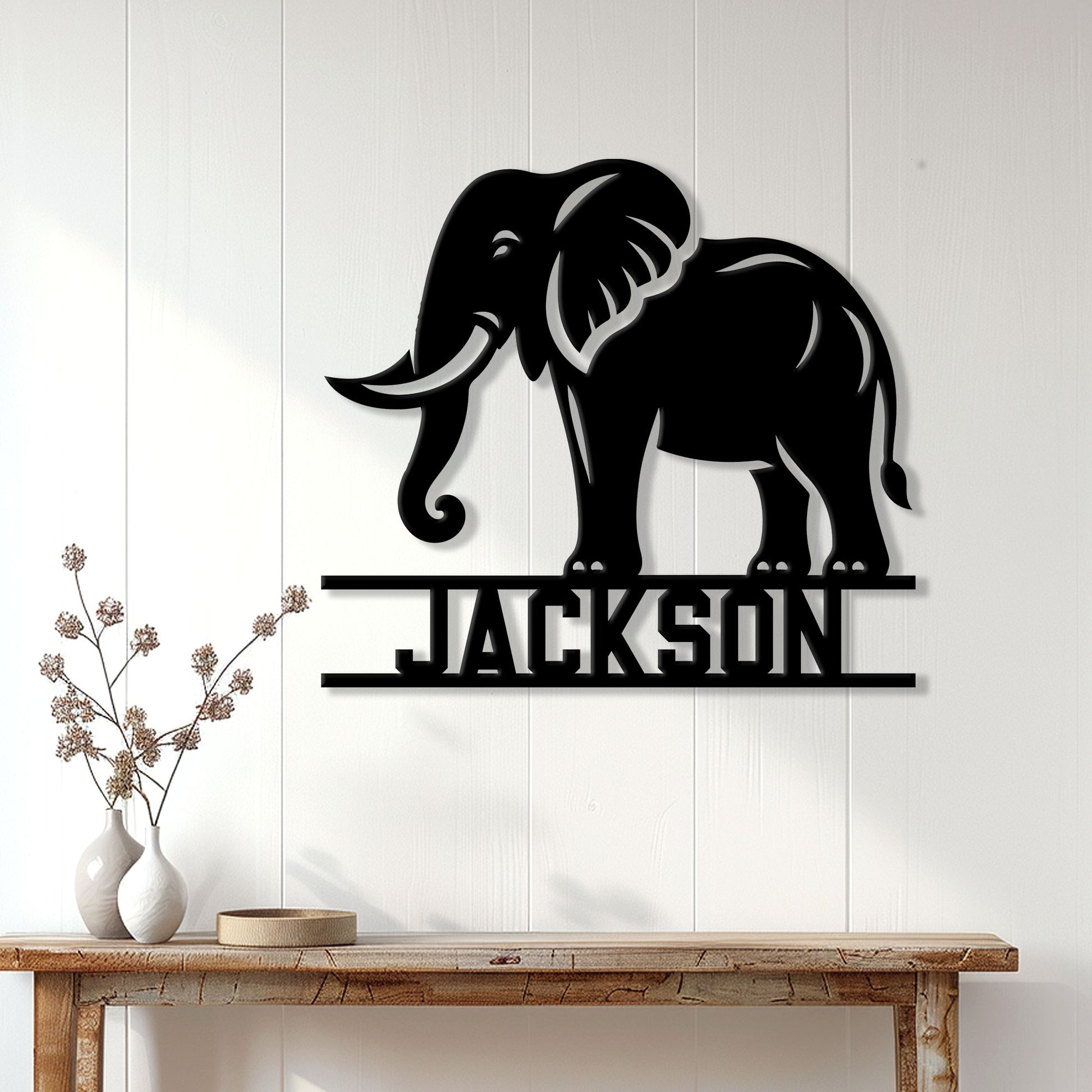 Black elephant silhouette sign displayed on a white paneled wall above a rustic console table