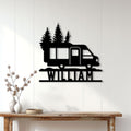 Black camper van and pine tree metal sign displayed on a white paneled wall in a cozy home