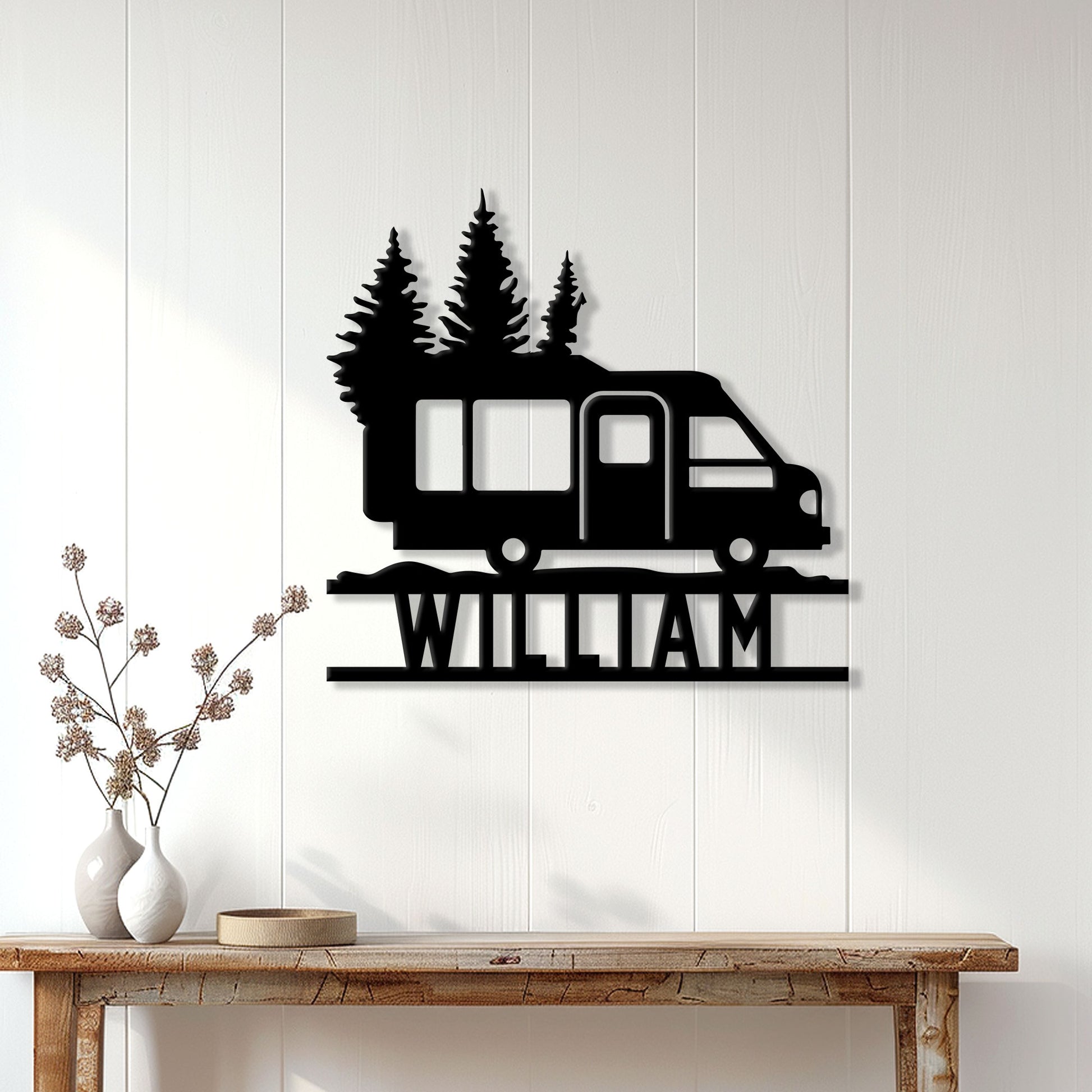 Black camper van and pine tree metal sign displayed on a white paneled wall in a cozy home