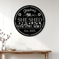 Floral She Shed metal sign displayed on a white paneled wall above a wooden console table