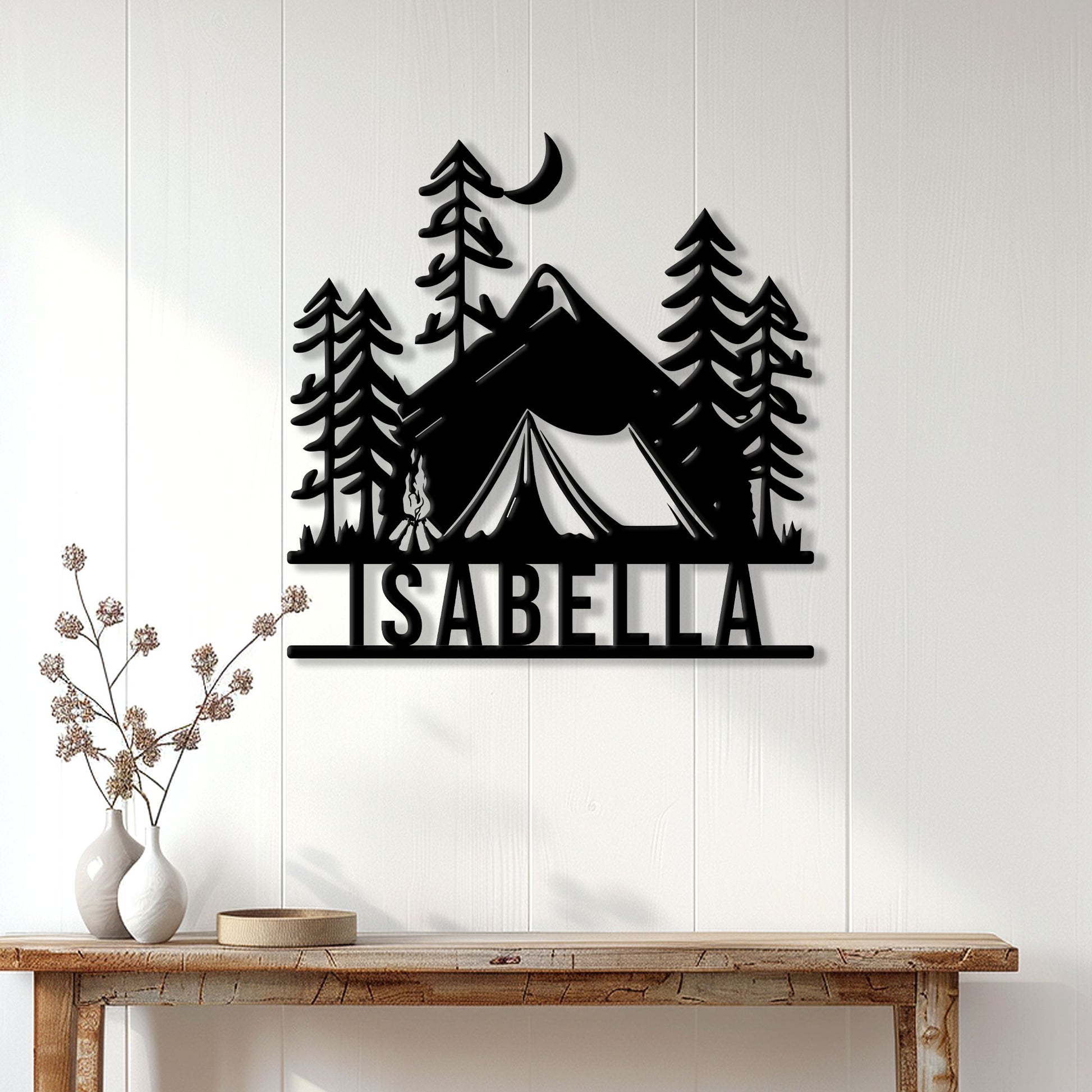 Black camping wall sign displayed on a white paneled wall above a rustic console table