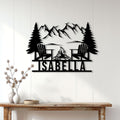 Camping wall decor displayed on a light wood wall, featuring chairs, pine trees, mountains, and a campfire
