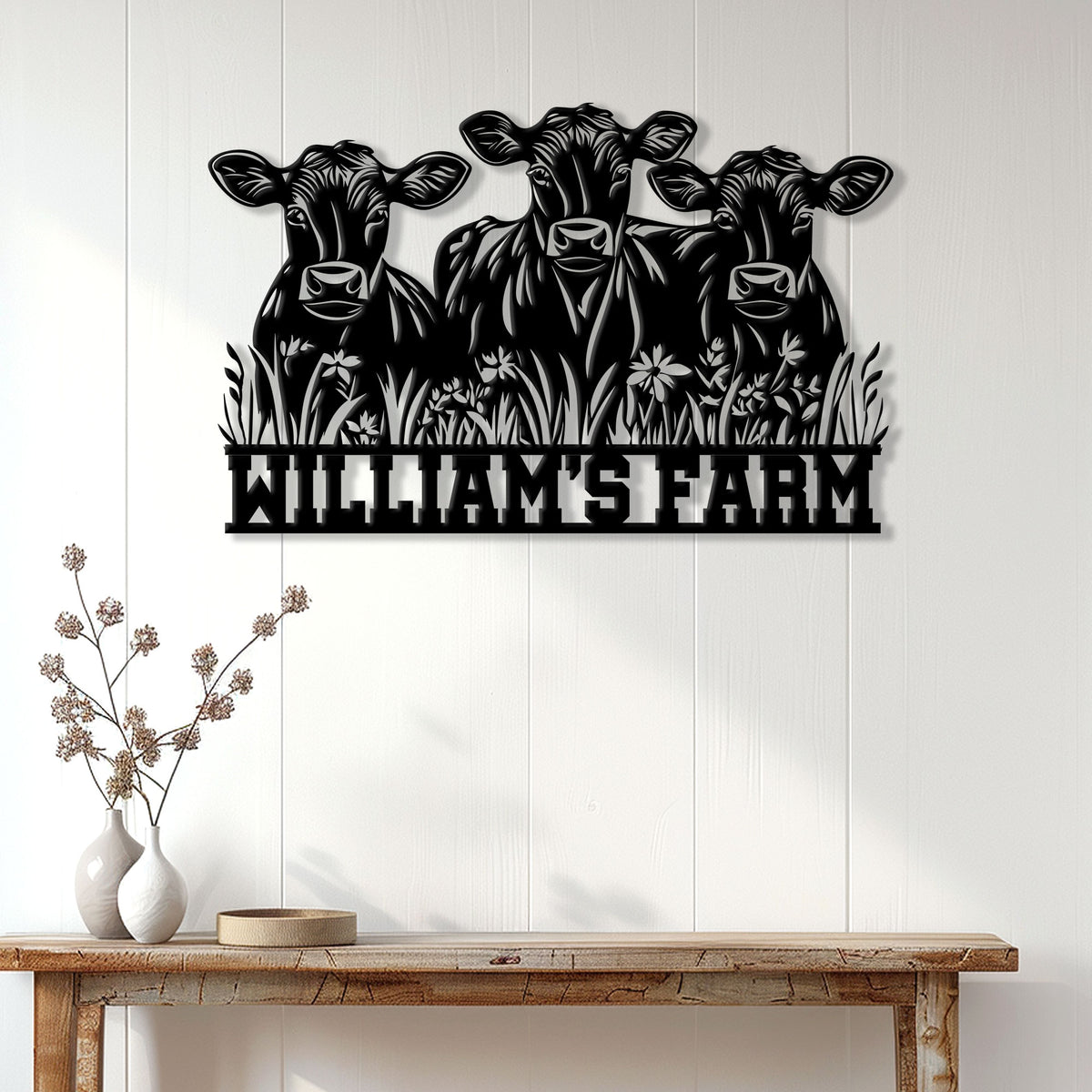 Three-cow metal farm sign displayed on a light farmhouse wall above a rustic console table