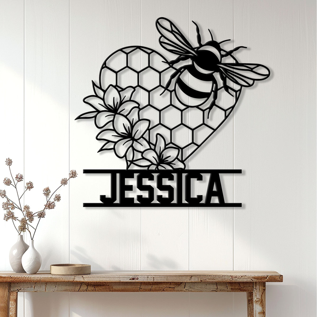 Bee metal wall decor displayed on a white paneled wall above a wood console with floral accents
