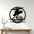 Black snowboarding wall sign displayed on a light wood-paneled wall above a console table