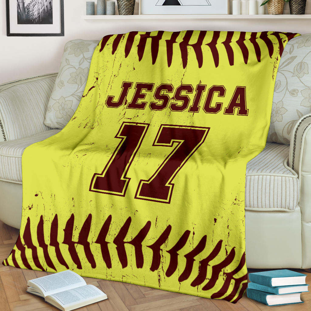 Softball throw blanket with bold yellow and burgundy ball-stitch artwork displayed on a living room sofa