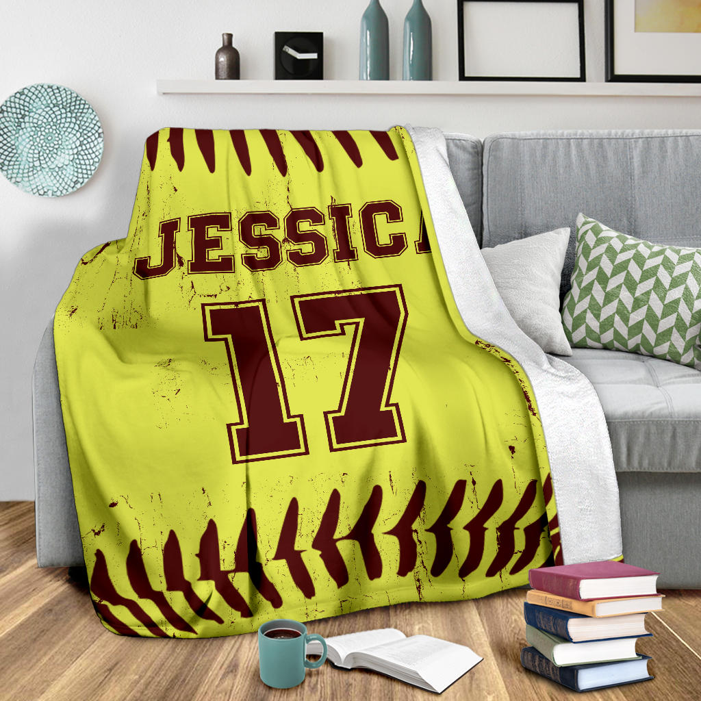 Custom softball throw blanket shown on a gray couch with bold sports artwork and ball-stitch borders