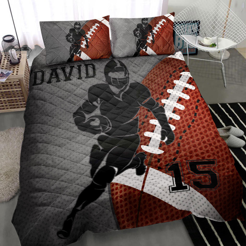 American football quilt blanket displayed on a bed with a helmeted player, football graphics, and gray and orange artwork