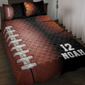 American football quilt blanket displayed on a bed with brown, black, and orange football artwork