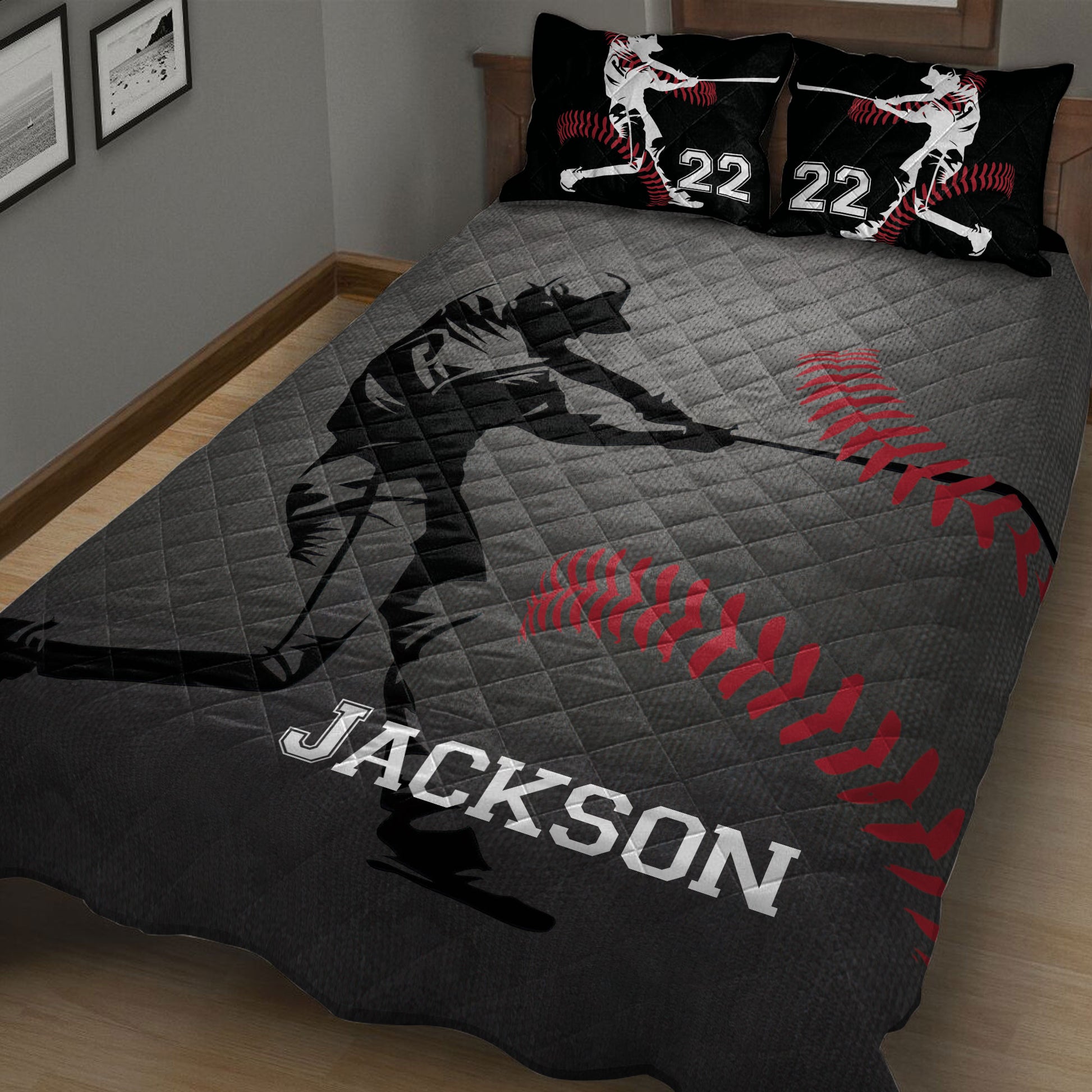 Close bedroom view of a baseball quilt blanket featuring a batter silhouette, red baseball stitching, and dark gray artwork