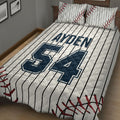 Close bedroom view of a baseball quilt blanket featuring bold navy sports graphics, pinstripes, and red stitching