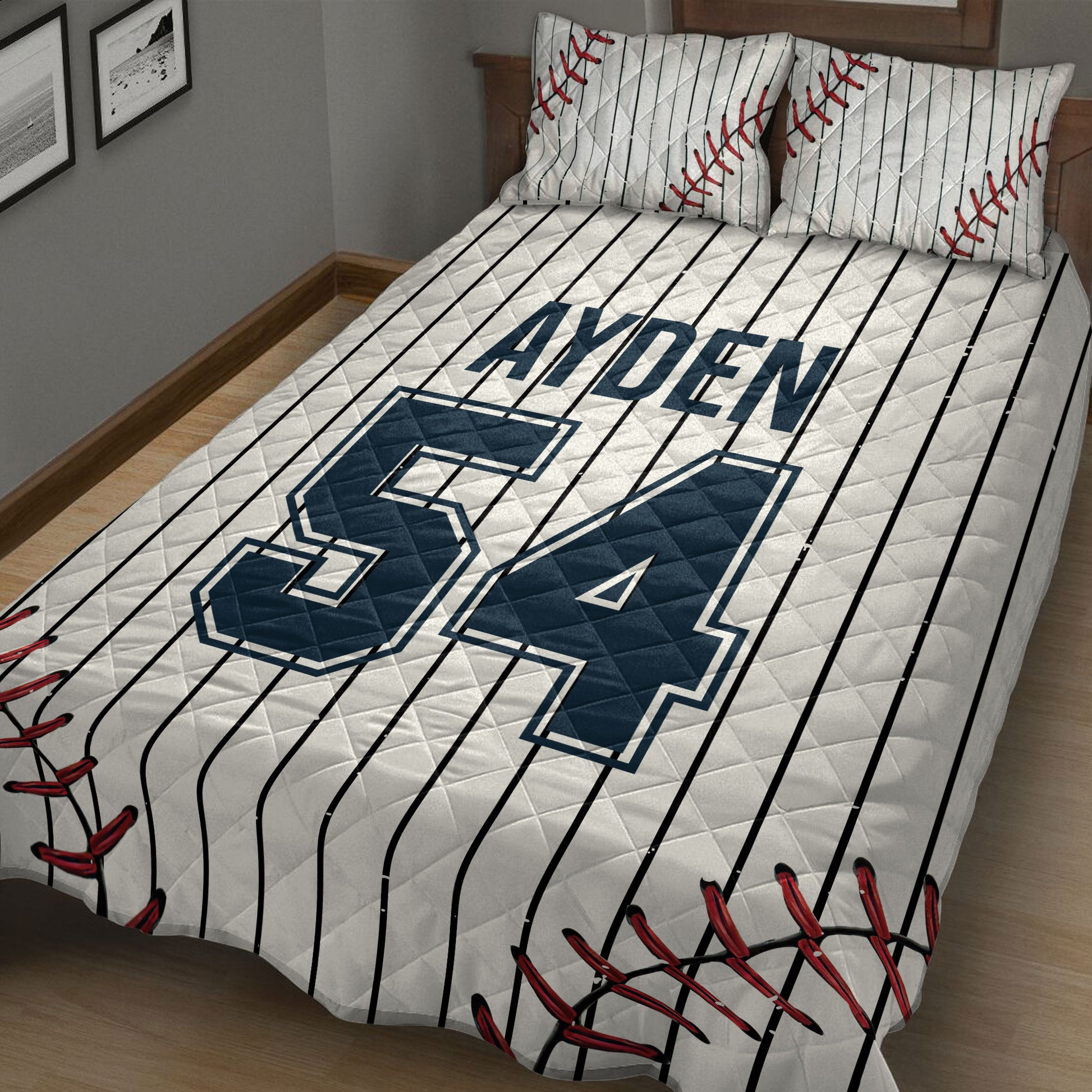 Close bedroom view of a baseball quilt blanket featuring bold navy sports graphics, pinstripes, and red stitching