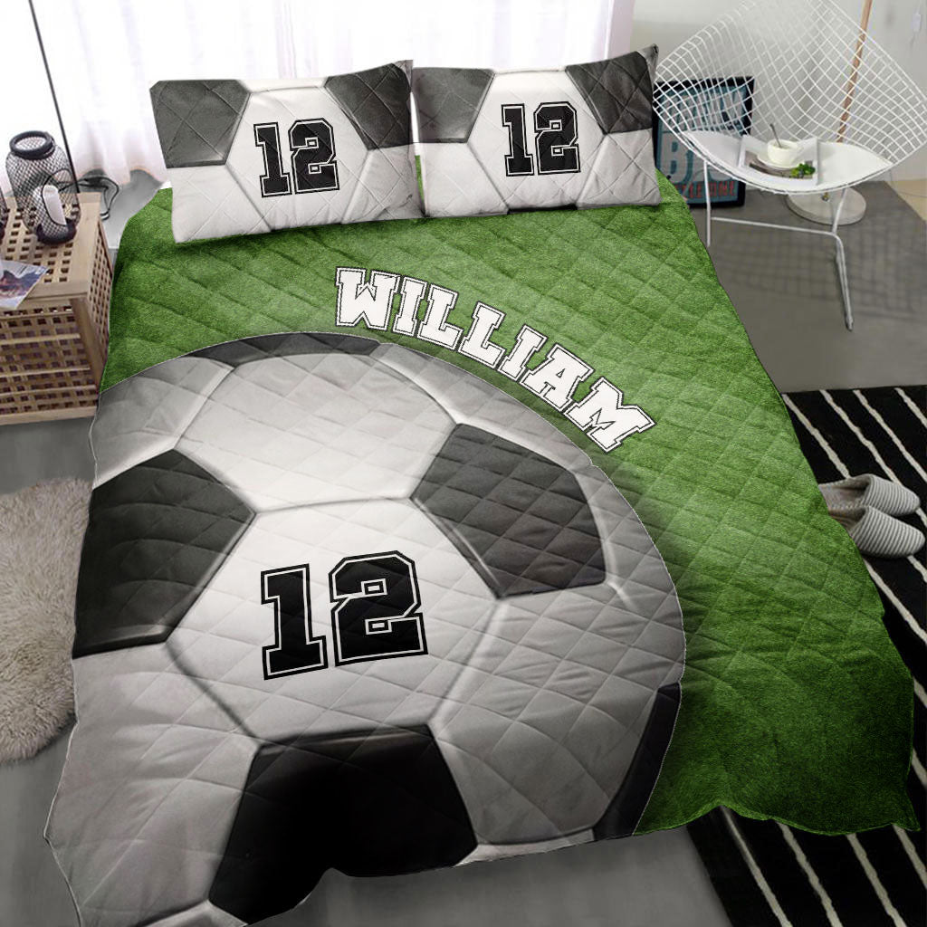 Soccer quilt blanket styled on a bed with a green field design and large soccer ball artwork