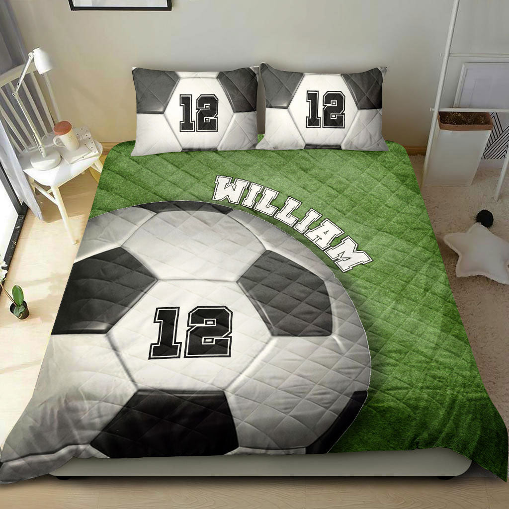 Soccer quilt bedding set displayed on a bed with green field artwork and matching soccer-themed pillows