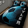 Close bedroom view of a dark soccer quilt blanket with blue ball artwork and varsity-style lettering